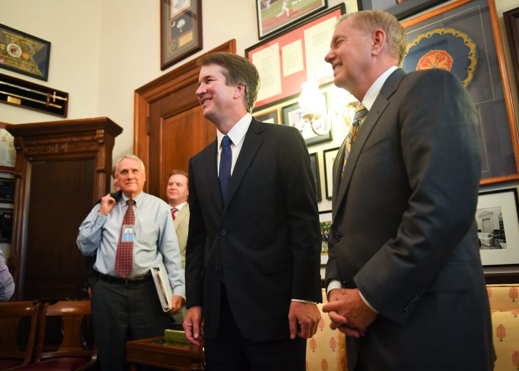 Supreme Court nominee Brett Kavanaugh and Sen. Lindsey Graham (R-SC), right, pose for the media in Graham's Russell Senate office before meeting on Capitol Hill in 2018. Former Sen. Jon Kyl (R-AZ), left, was escorting the nominee around Capitol Hill.